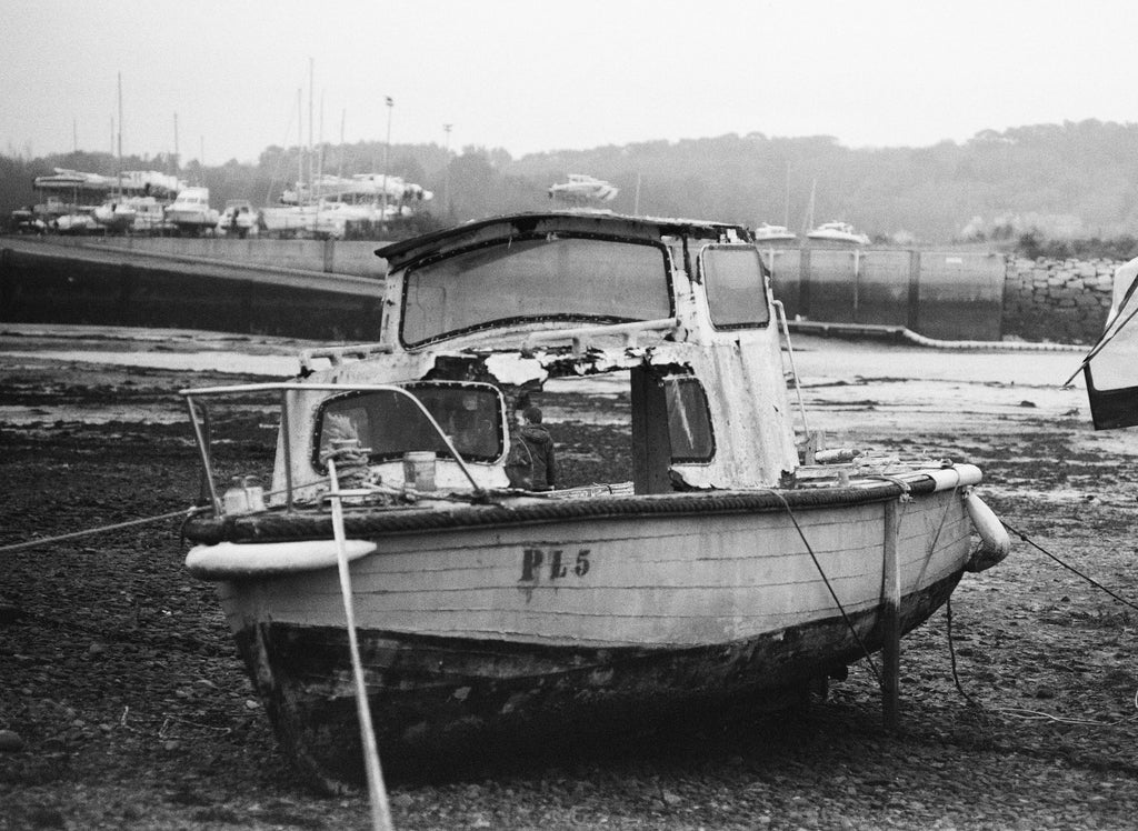 Vieux bateau de pêche PL5 échoué sur la vase à marée basse dans un port brumeux, argentique noir et blanc