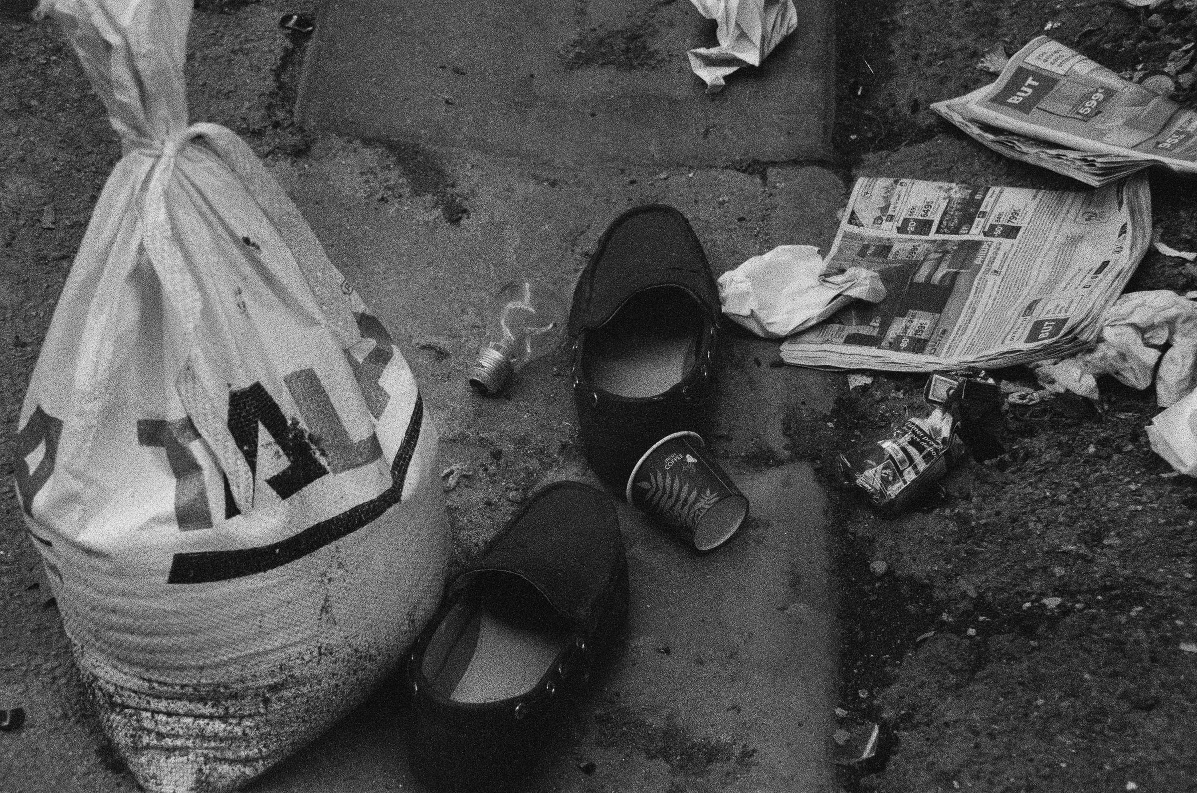 Chaussures abandonnées et débris urbains sur pavé mouillé, photographie documentaire noir et blanc