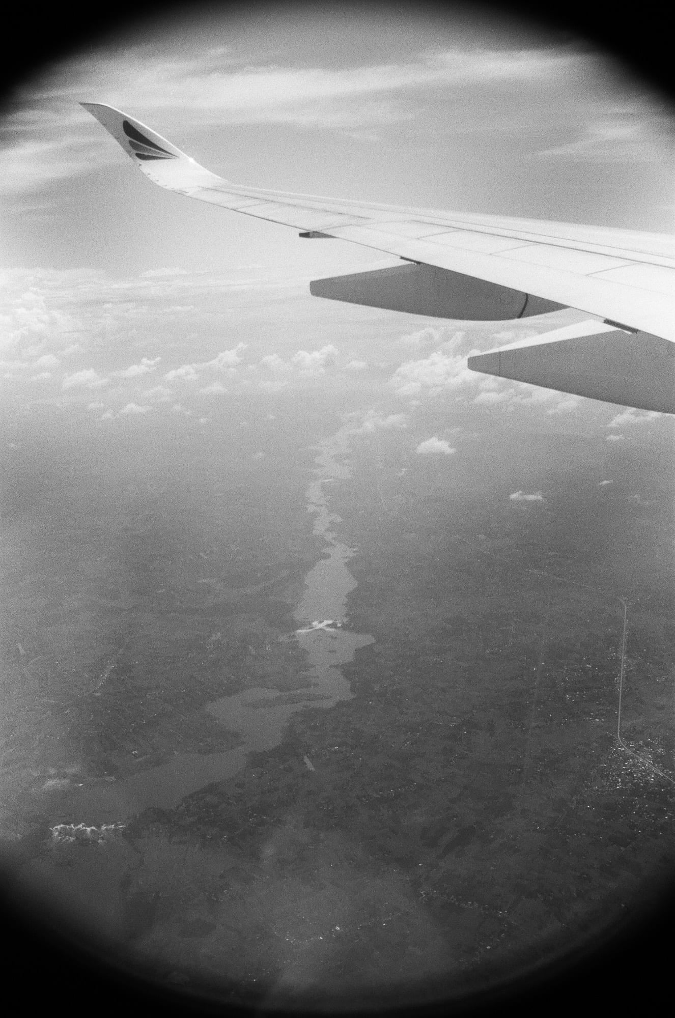 Vue aérienne à travers un hublot d'avion sur l'aile et une rivière sinueuse en contrebas, photographie argentique noir et blanc