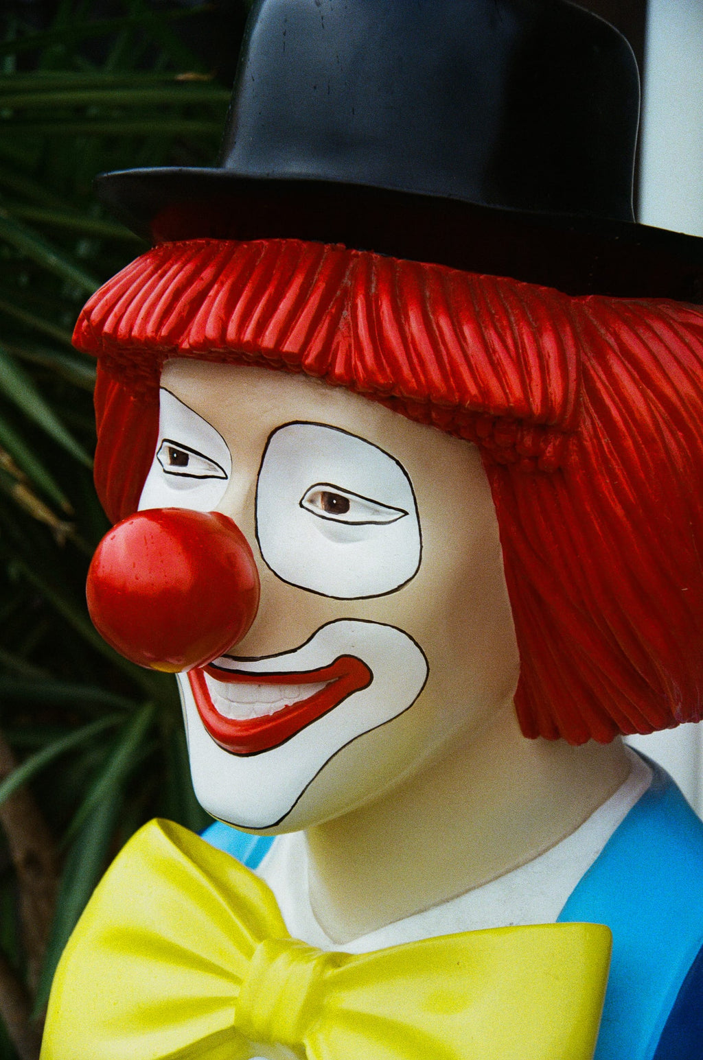 Portrait en gros plan d'une statue de clown peinte aux cheveux rouges et nœud papillon jaune, argentique couleur vif