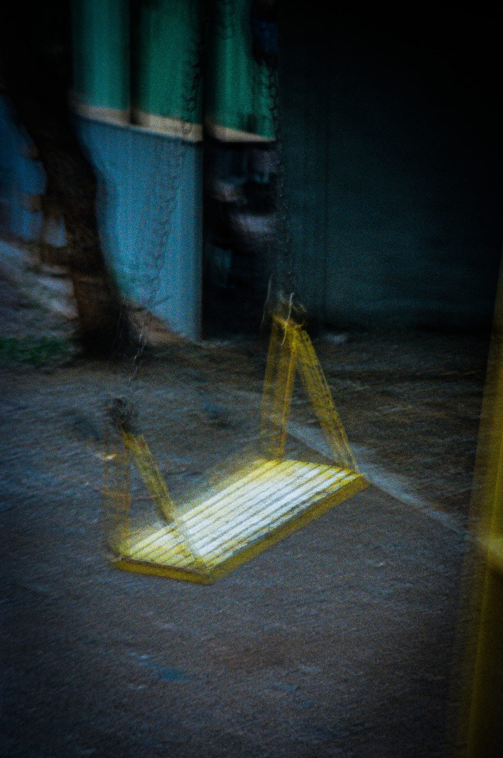 Balançoire jaune en surimpression spectrale dans une ruelle urbaine bleue, photographie argentique couleur
