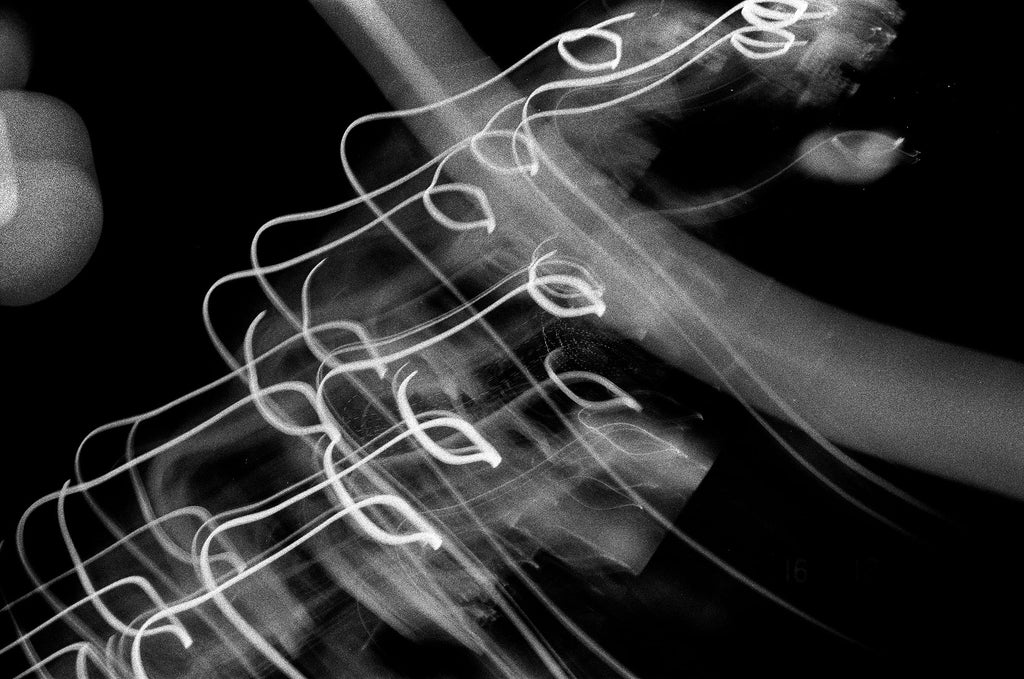 Longue exposition de cordes de guitare créant des traînées de lumière lumineuses dans l'obscurité, photographie argentique noir et blanc