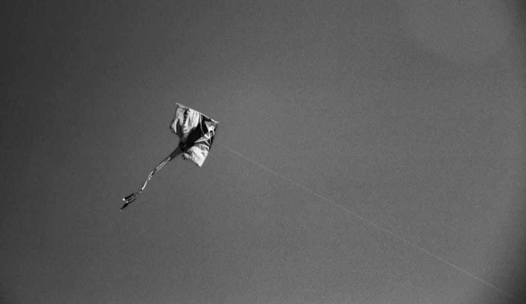 Cerf-volant solitaire dans un ciel gris traversé par une traînée d'avion, minimaliste noir et blanc argentique
