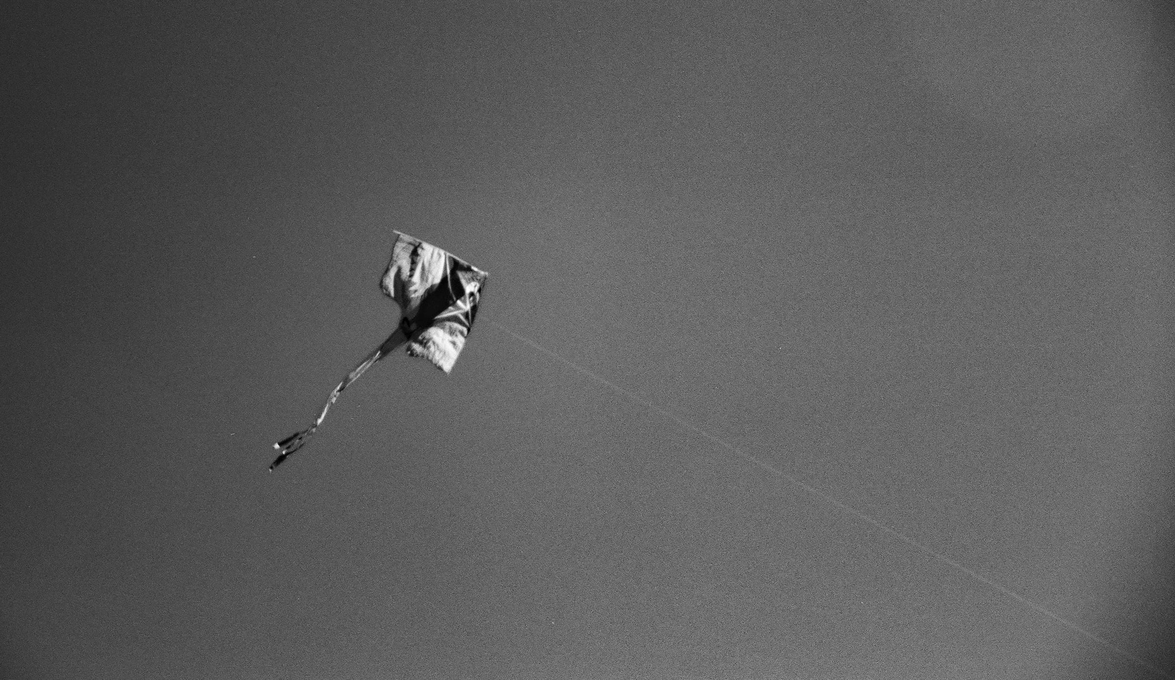 Cerf-volant solitaire dans un ciel gris traversé par une traînée d'avion, minimaliste noir et blanc argentique