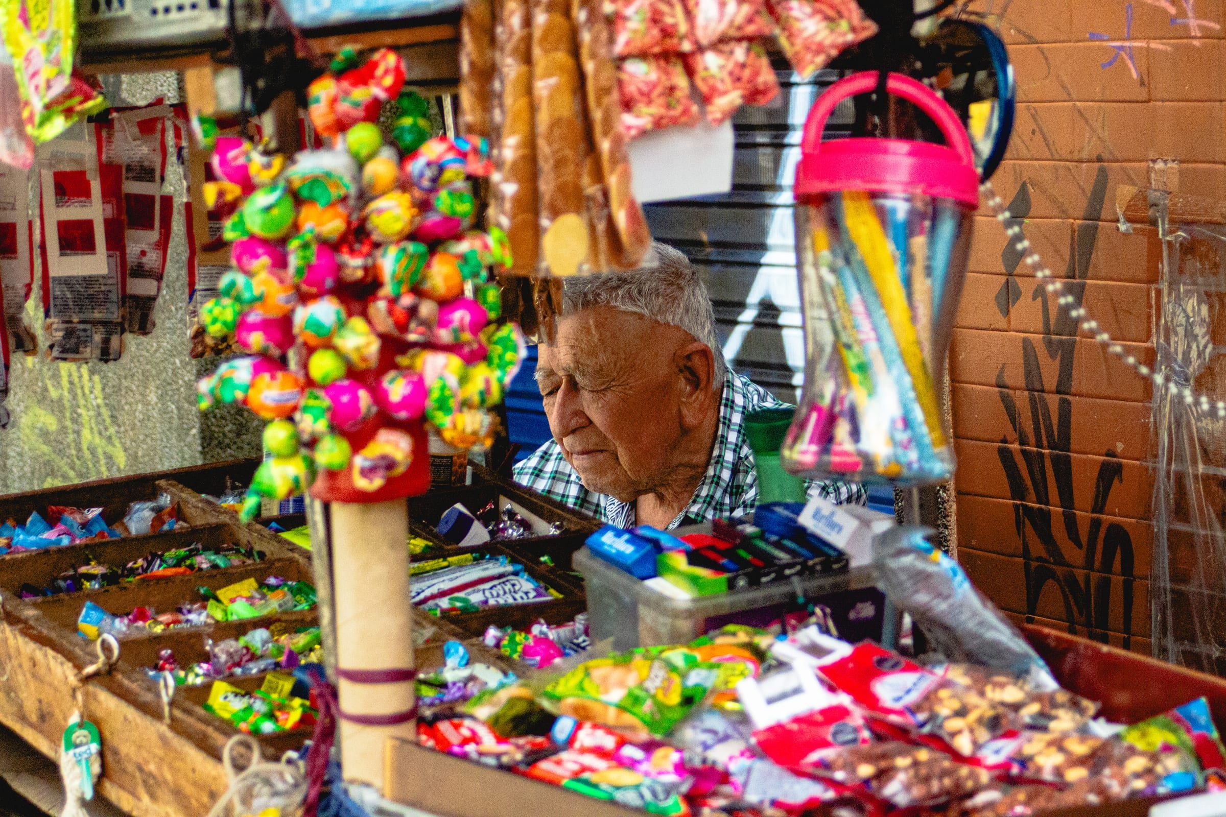 Vendeur de bonbons âgé se reposant à un étal de marché coloré débordant de sucreries et sucettes à Medellín, portrait documentaire