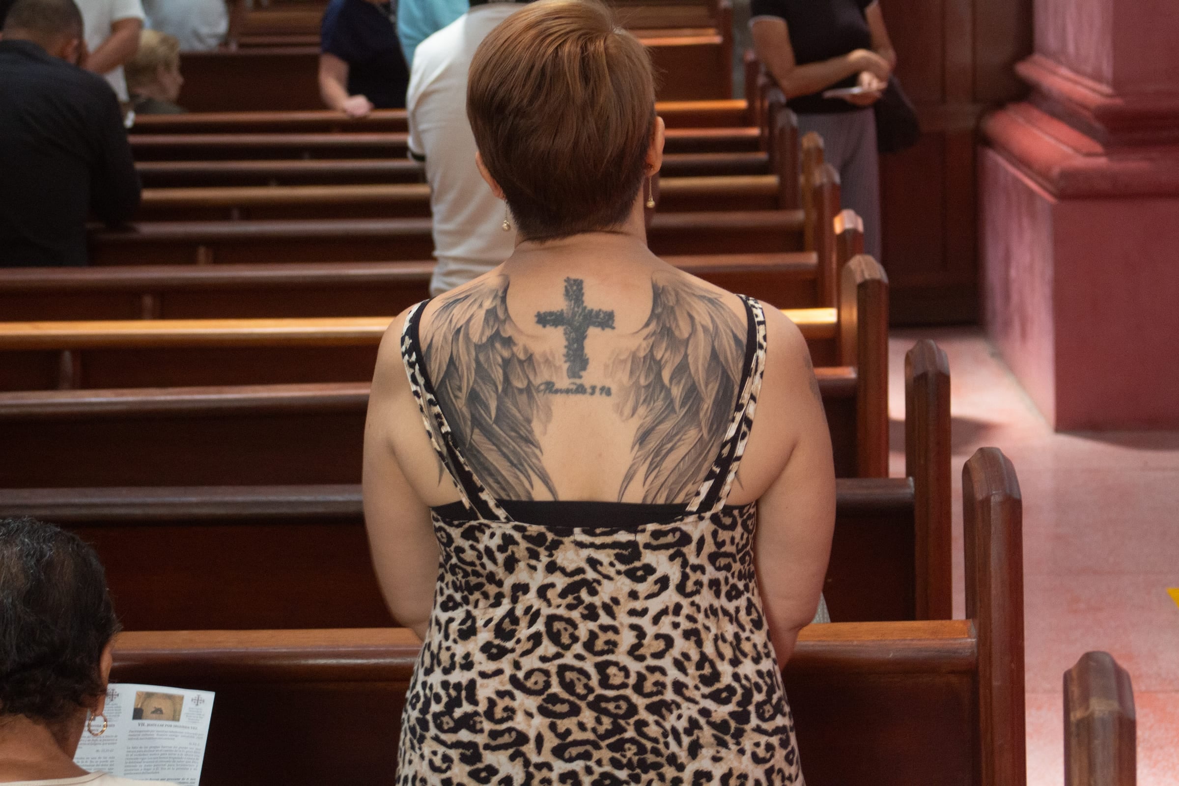 Plan rapproché sur le cou et le dos tatoués d'un homme, croix et ailes, portrait documentaire dévotionnel, Medellín
