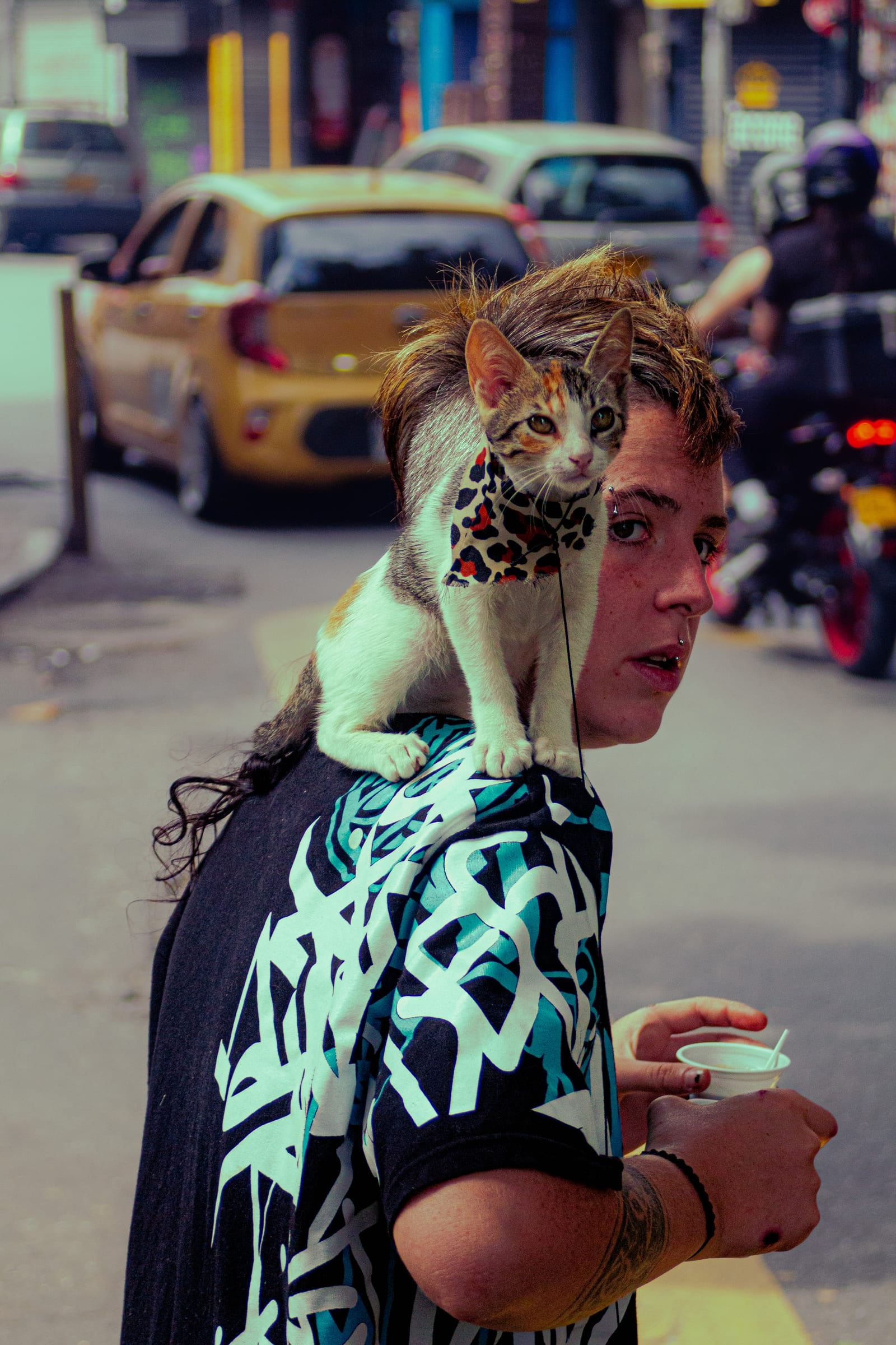 Jeune personne portant un chaton en harnais léopard sur l'épaule dans une rue colorée de Medellín, documentaire couleur
