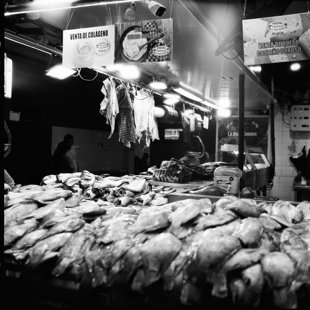 Vendeur de marché se reposant parmi des sacs de grain empilés, photographie documentaire noir et blanc, Colombie
