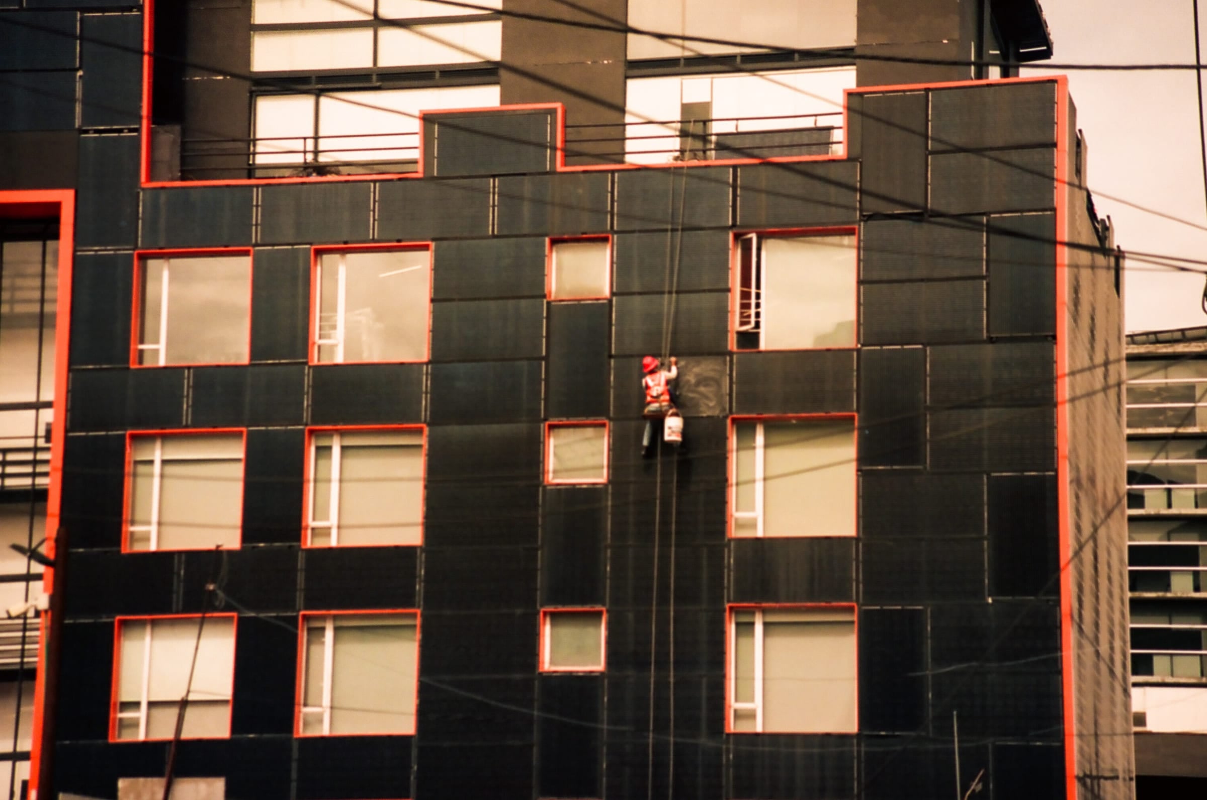 Ouvrier en rappel sur la façade d'un immeuble à Medellín, photographie documentaire sur le travail urbain