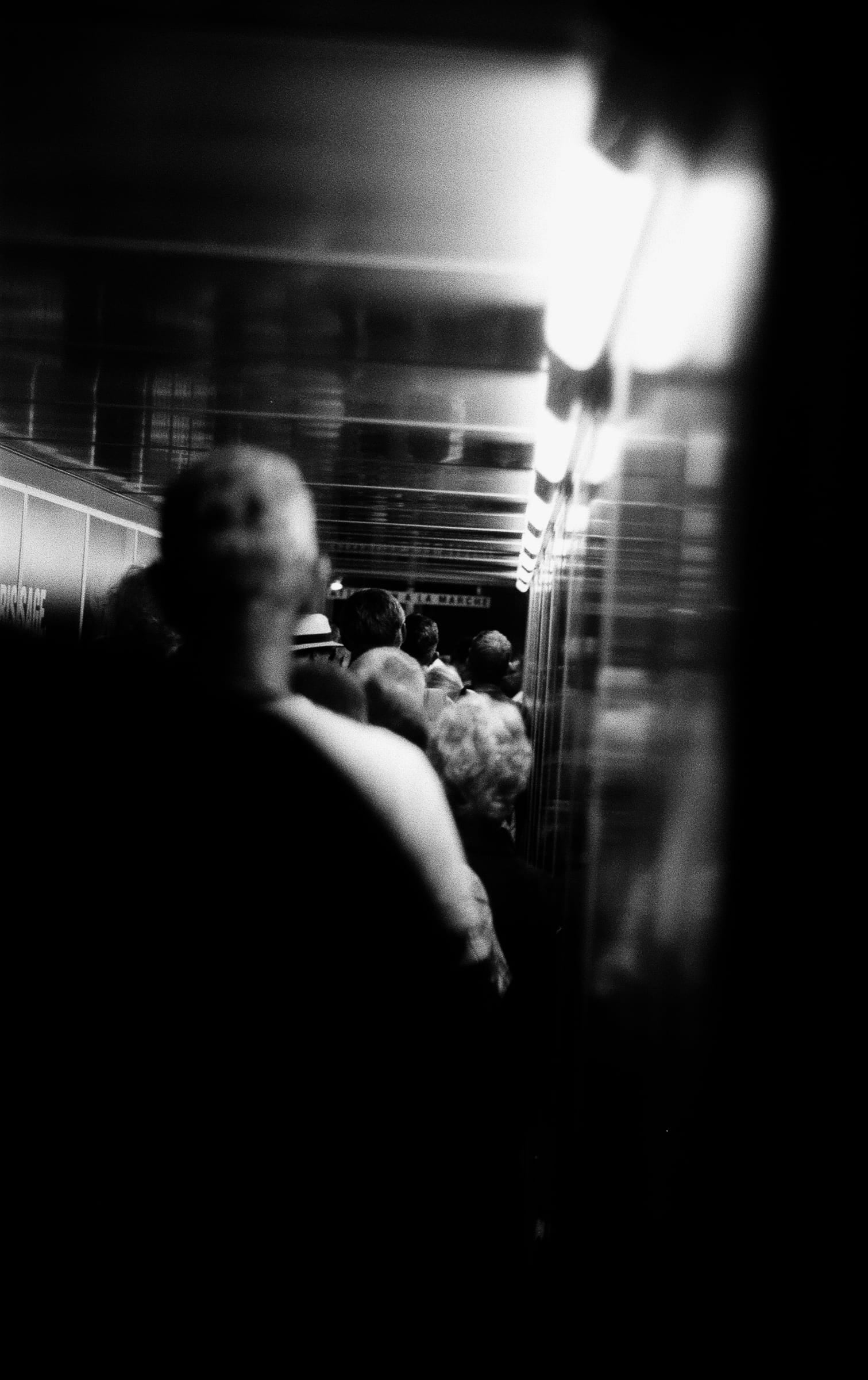 Foule de passagers du métro entrevue à travers une fente sombre verticale avec lumière vive, photographie urbaine argentique noir et blanc
