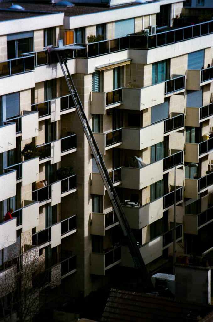 Monte-meuble s'étendant en diagonale sur la façade d'un immeuble parisien, photographie urbaine argentique couleur