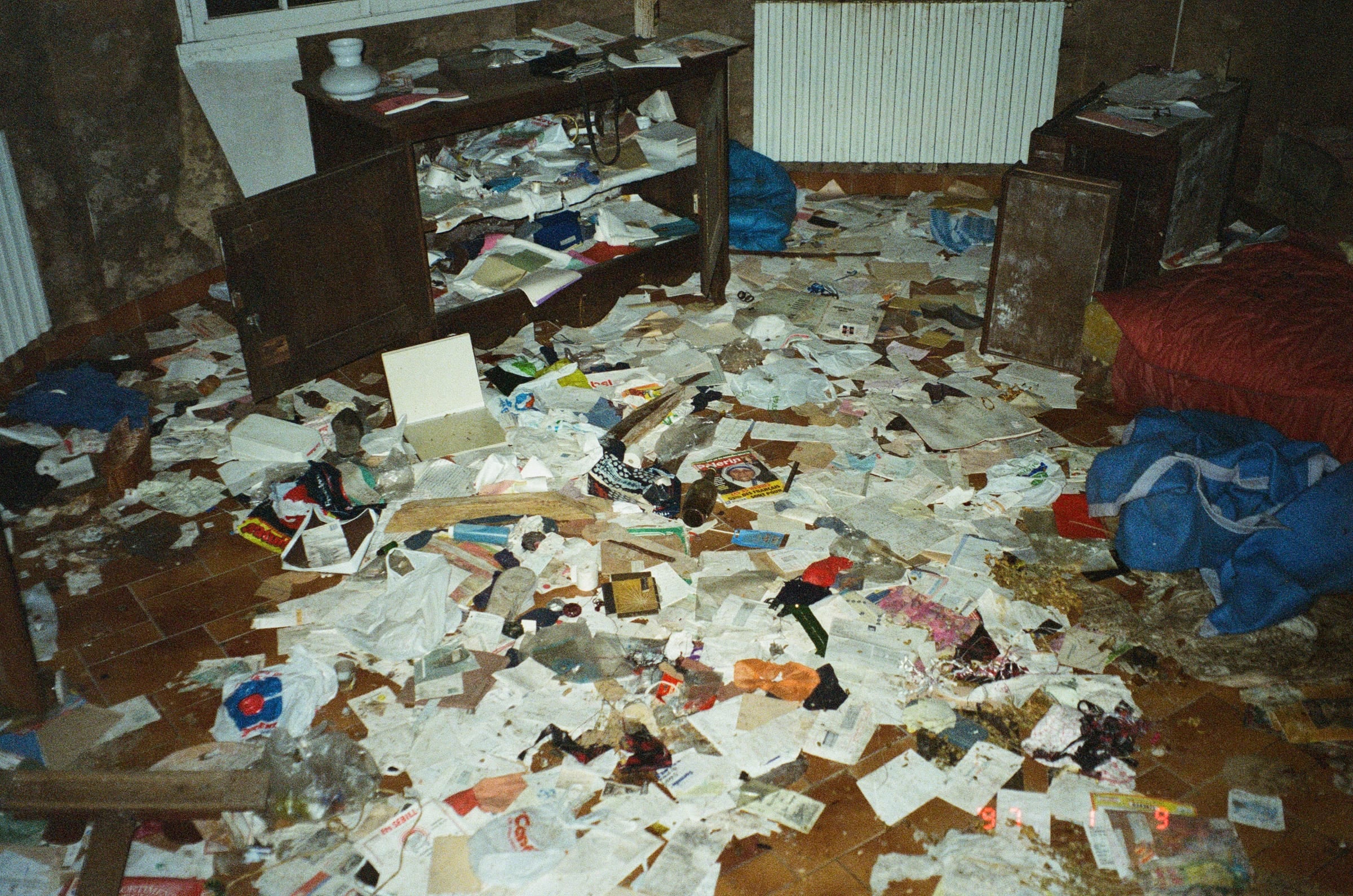 Intérieur d'une pièce entièrement saccagée couverte de papiers épars et débris, photographie documentaire argentique couleur