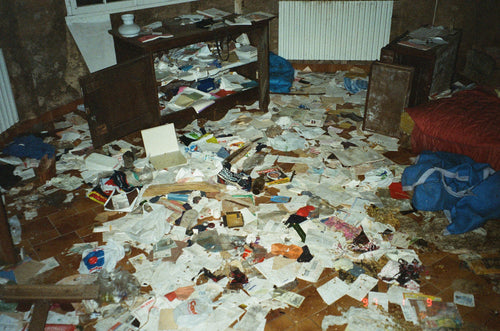 Intérieur d'une pièce entièrement saccagée couverte de papiers épars et débris, photographie documentaire argentique couleur