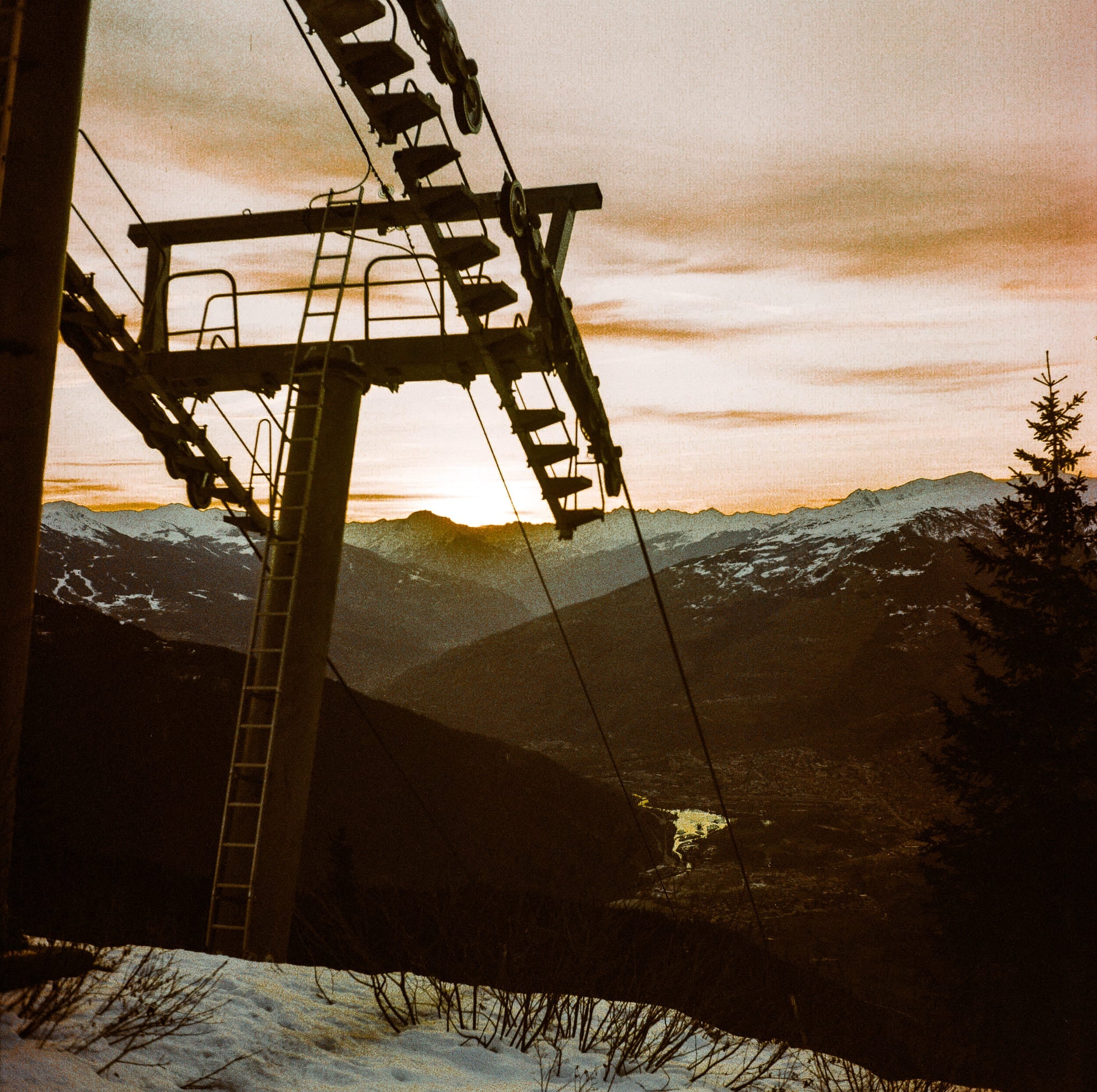 Silhouette de télésiège contre un coucher de soleil alpin doré et chaîne de montagnes enneigées, argentique