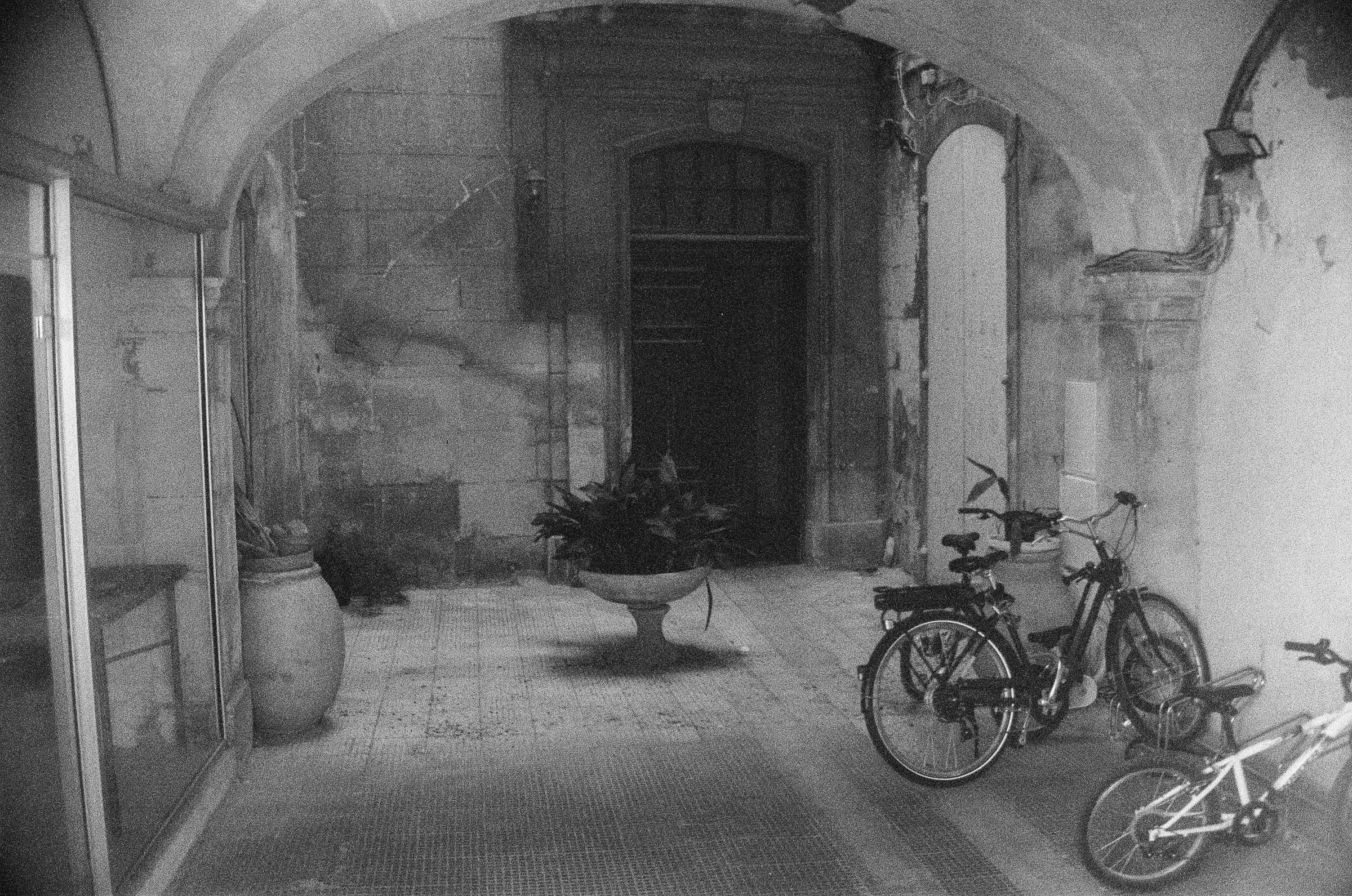 Couloir voûté en pierre en perspective fuyante avec vélos garés et urne ancienne la nuit, photographie architecturale argentique noir et blanc