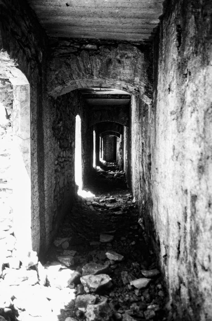 Couloir en pierre ancienne en ruines avec arches répétées créant un point de fuite, argentique noir et blanc