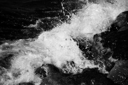 Eau en cascade et éclaboussures sur des rochers sombres, photographie de texture argentique noir et blanc